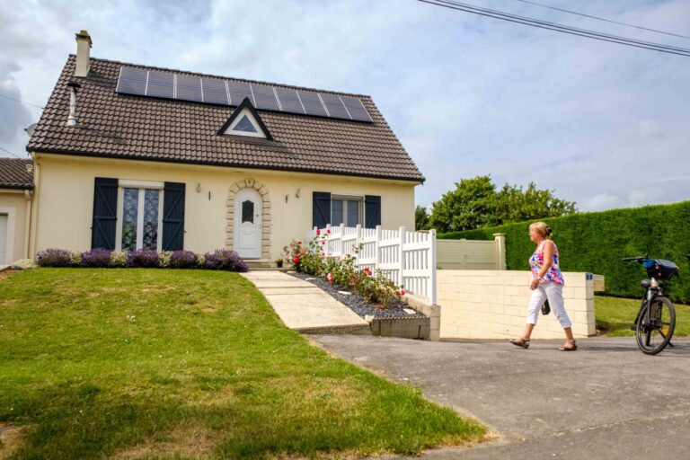 Femme rentrant d'une balade à vélo électrique dans sa maison avec panneaux solaires